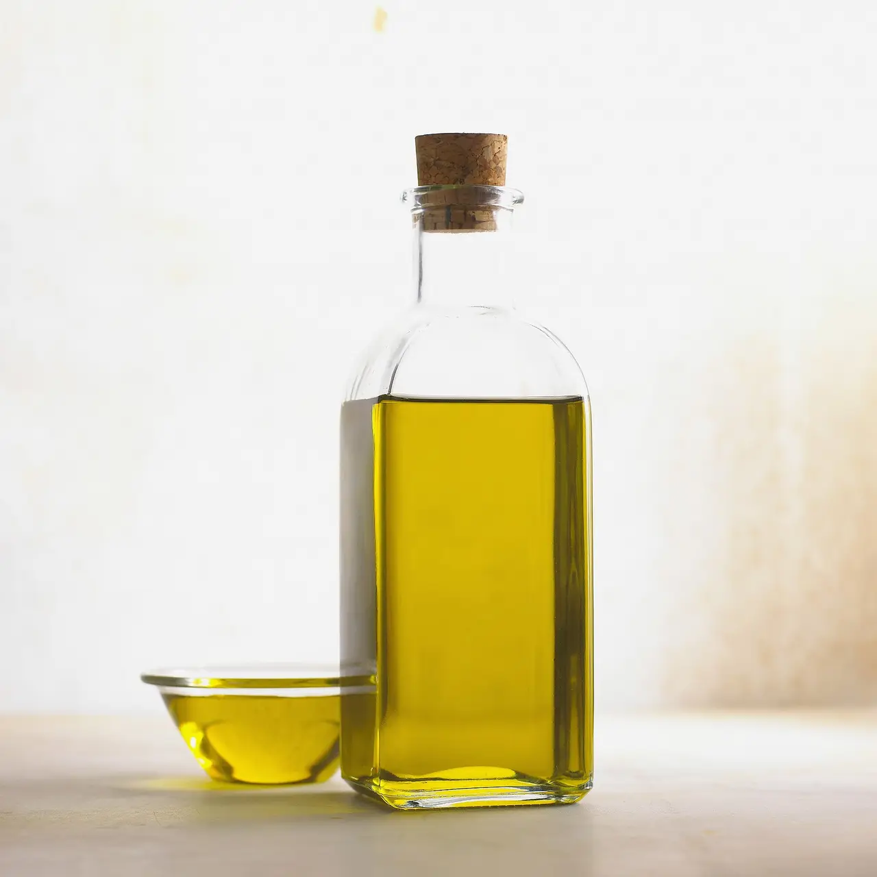 A glass bottle of olive oil with a cork next to a small dish of oil