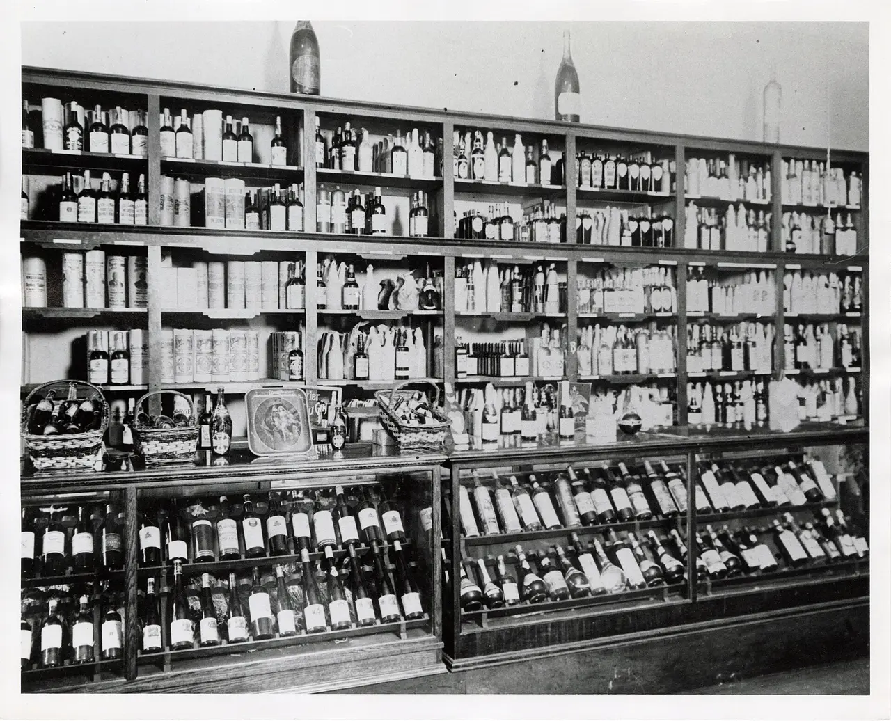 An old black and white photo of shop shelves lined with bottles