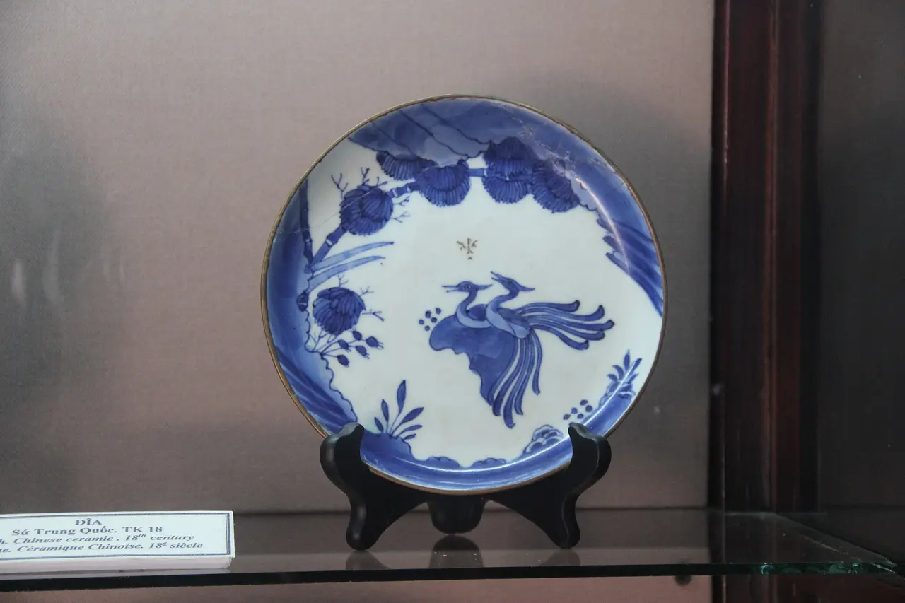A blue and white plate painted with a bird on a black display stand