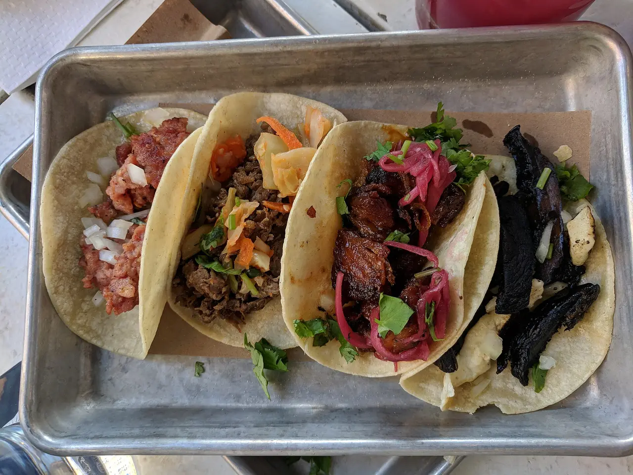 Four filled tacos on a metal tray