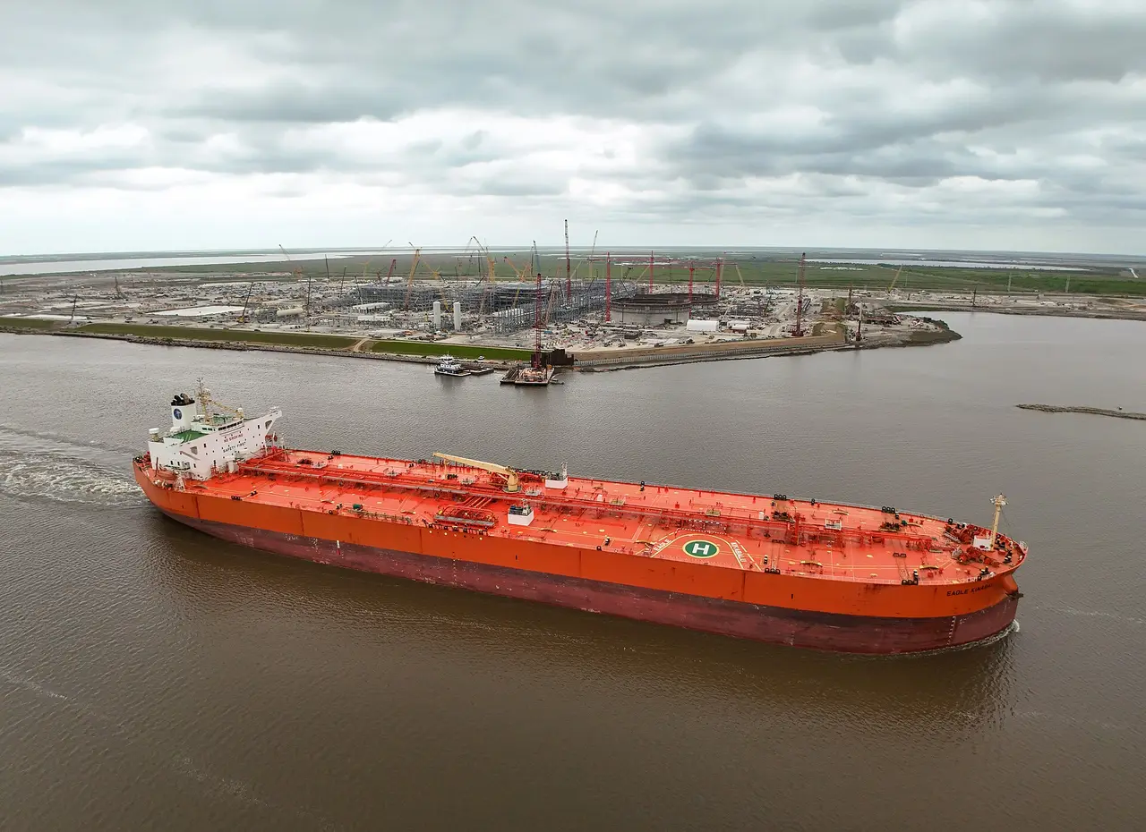 A red crude oil tanker on a river under a cloudy sky