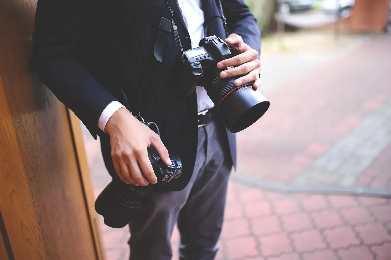 A man holding two cameras on a brick pavement