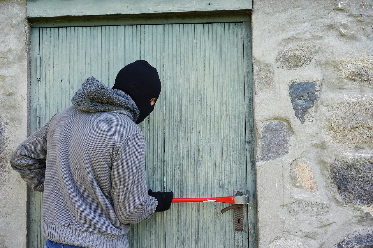A hooded man in a balaclava levering a door open with a crowbar