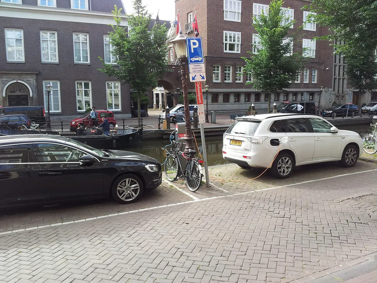 Two electric cars plugged in at a canalside charging station