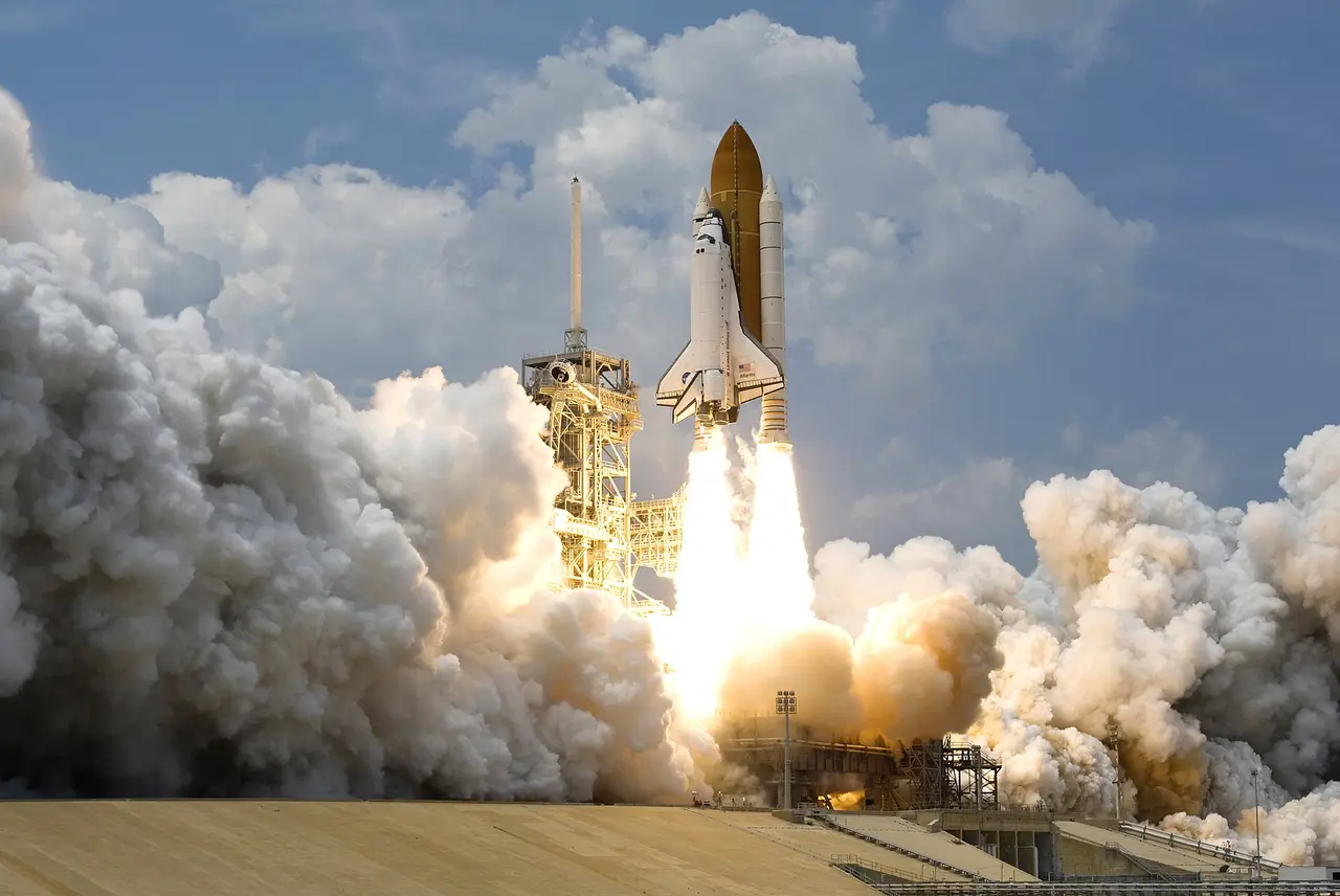 Space shuttle lifting off from its pad amid large clouds of exhaust
