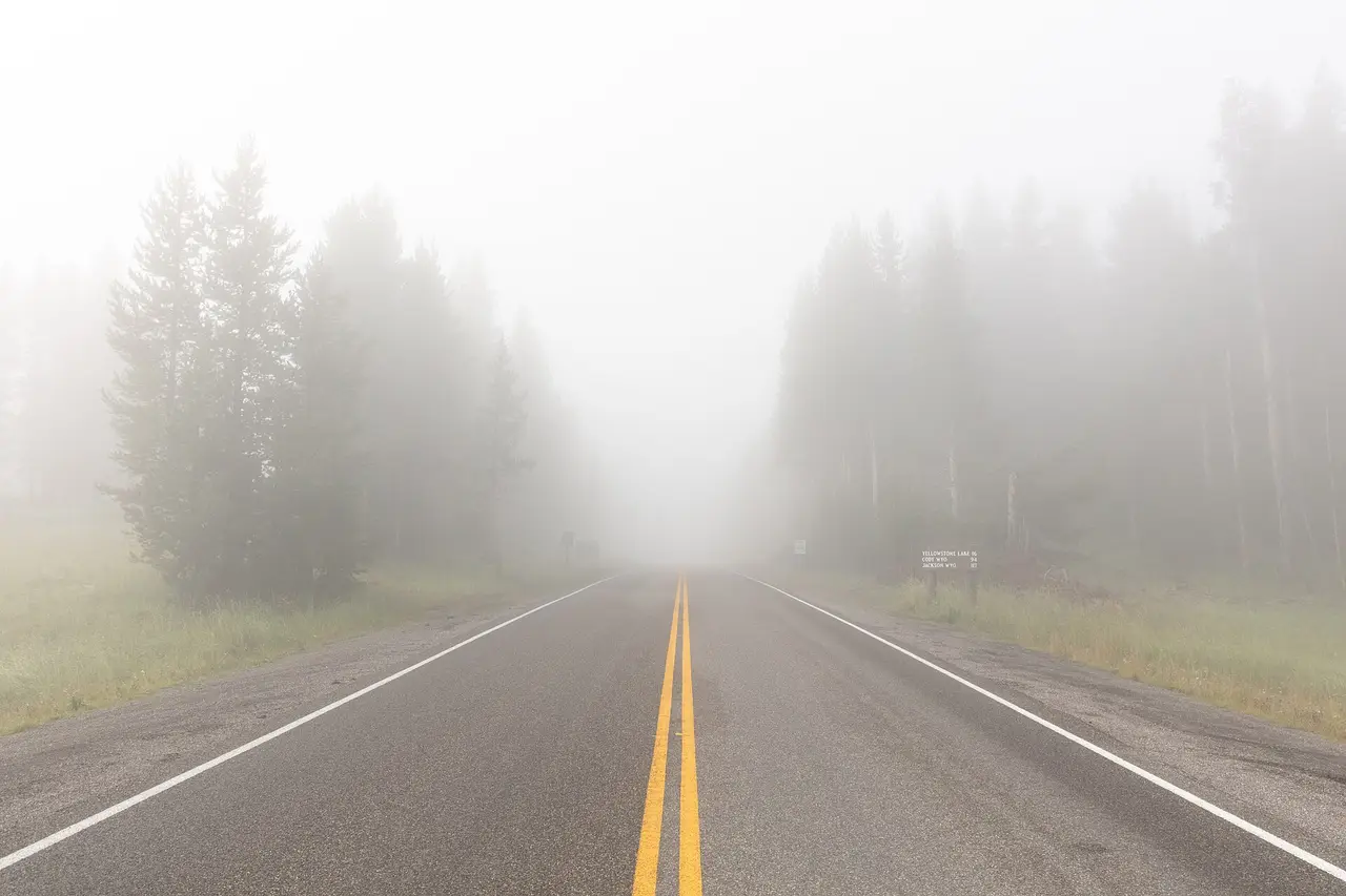 Straight road with yellow centre lines disappearing into thick fog