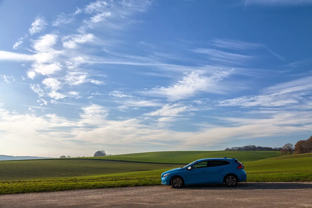 Blue car beside green fields under a blue sky