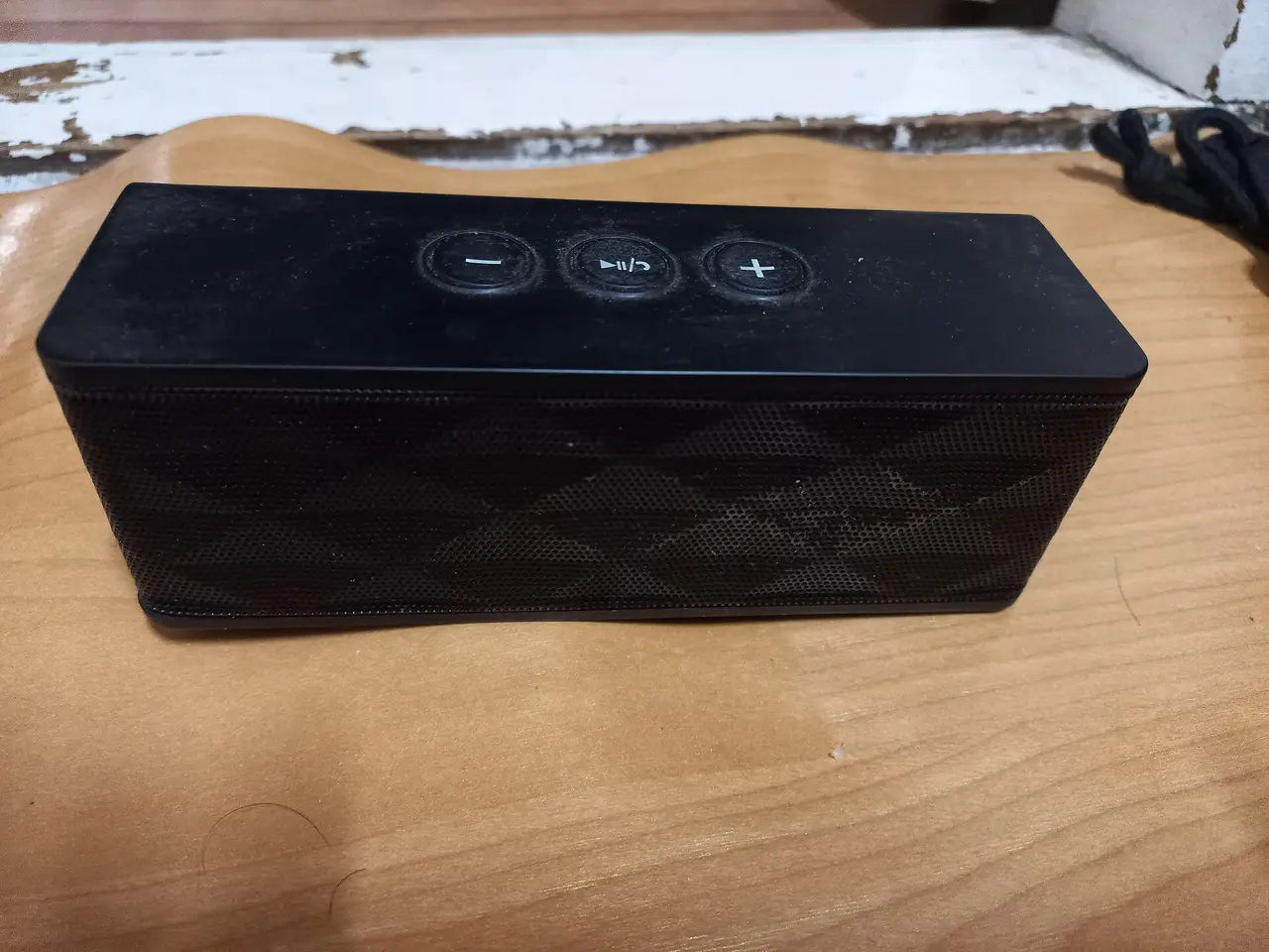 Black rectangular portable speaker with three buttons on a wooden table