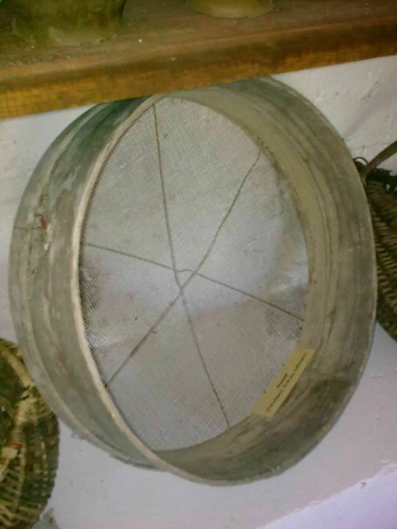 Round wooden-framed sieve with fine mesh hanging on a wall