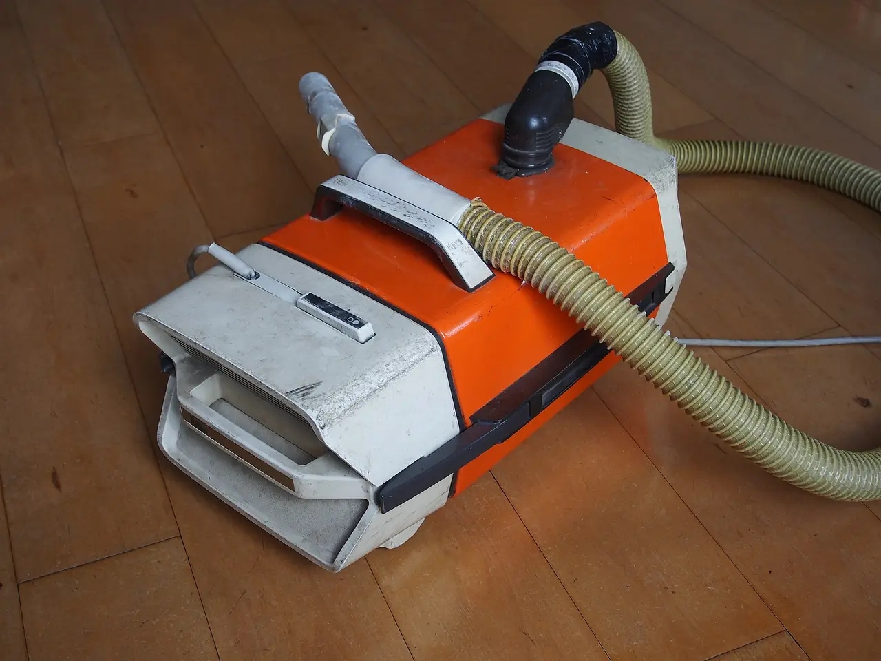 An orange and grey canister vacuum cleaner with hose