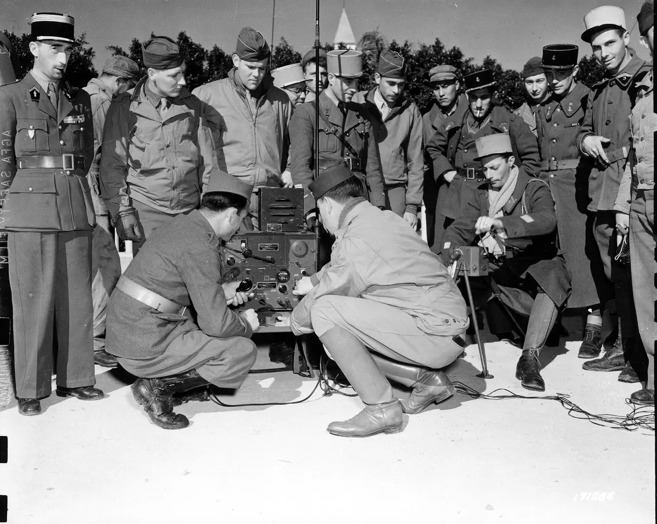 Uniformed men crouching around a hand-cranked radio set outdoors
