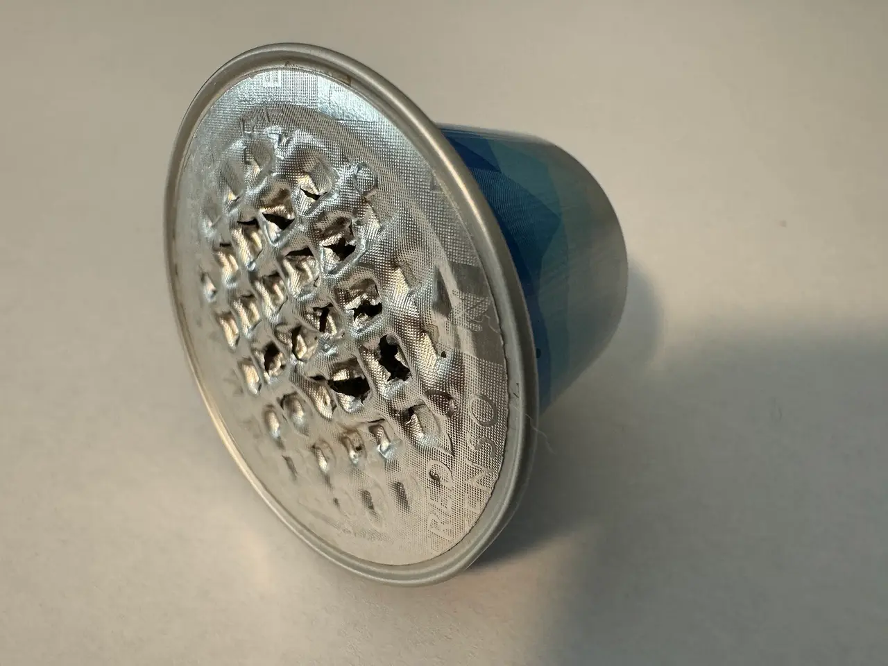 Aluminium coffee capsule with a perforated lid on a grey surface