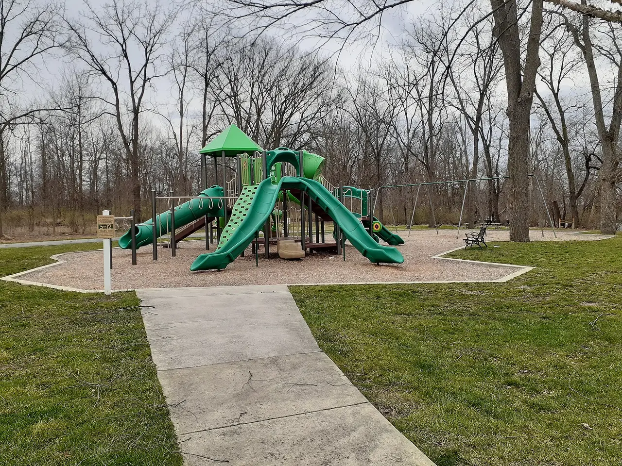 Empty playground with green slides on a lawn among bare trees