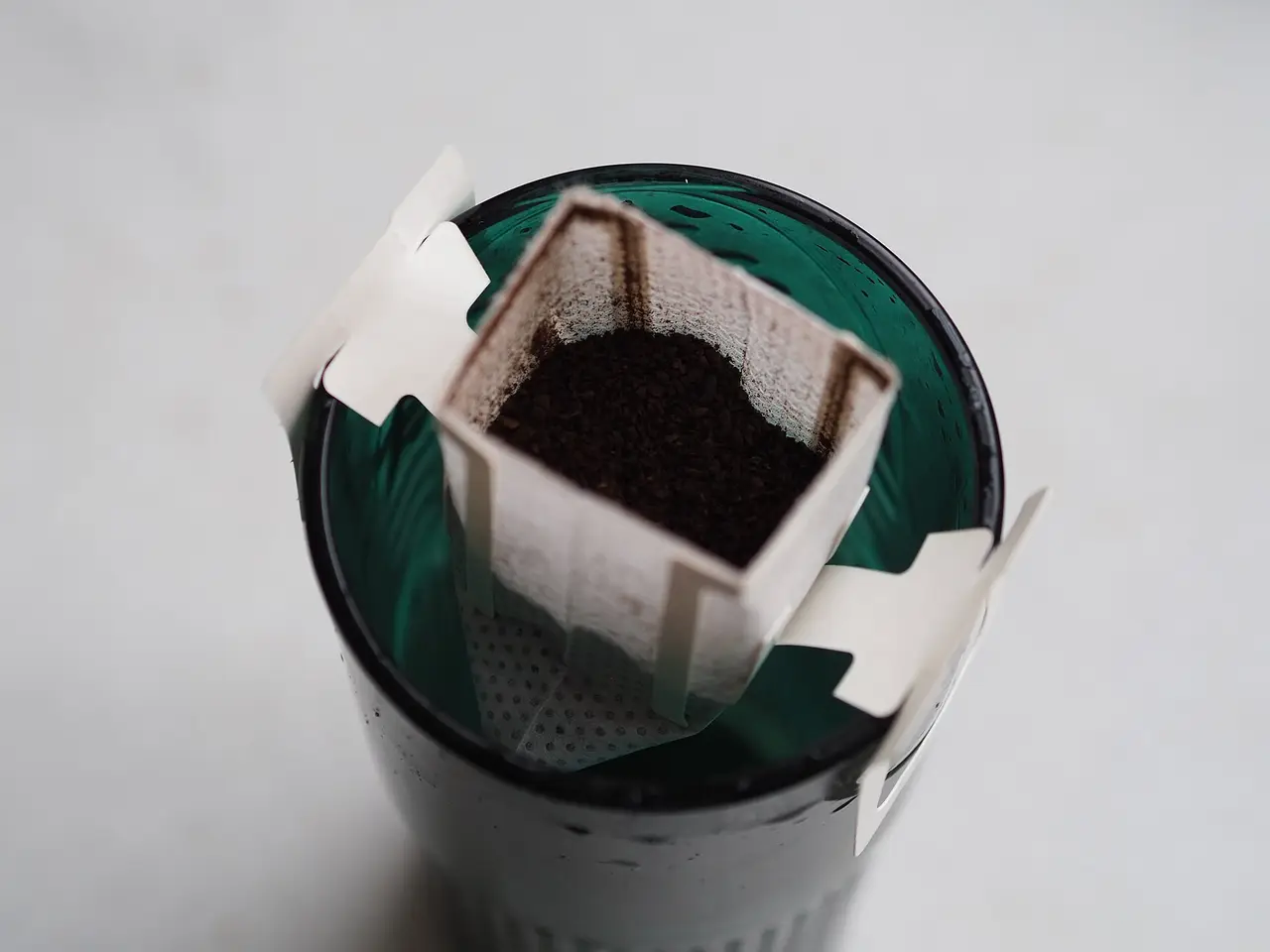 A coffee filter bag filled with grounds resting on a cup