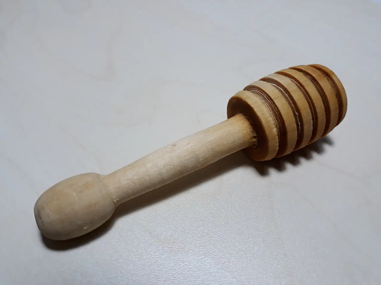 Wooden honey dipper with a ridged head on a grey surface