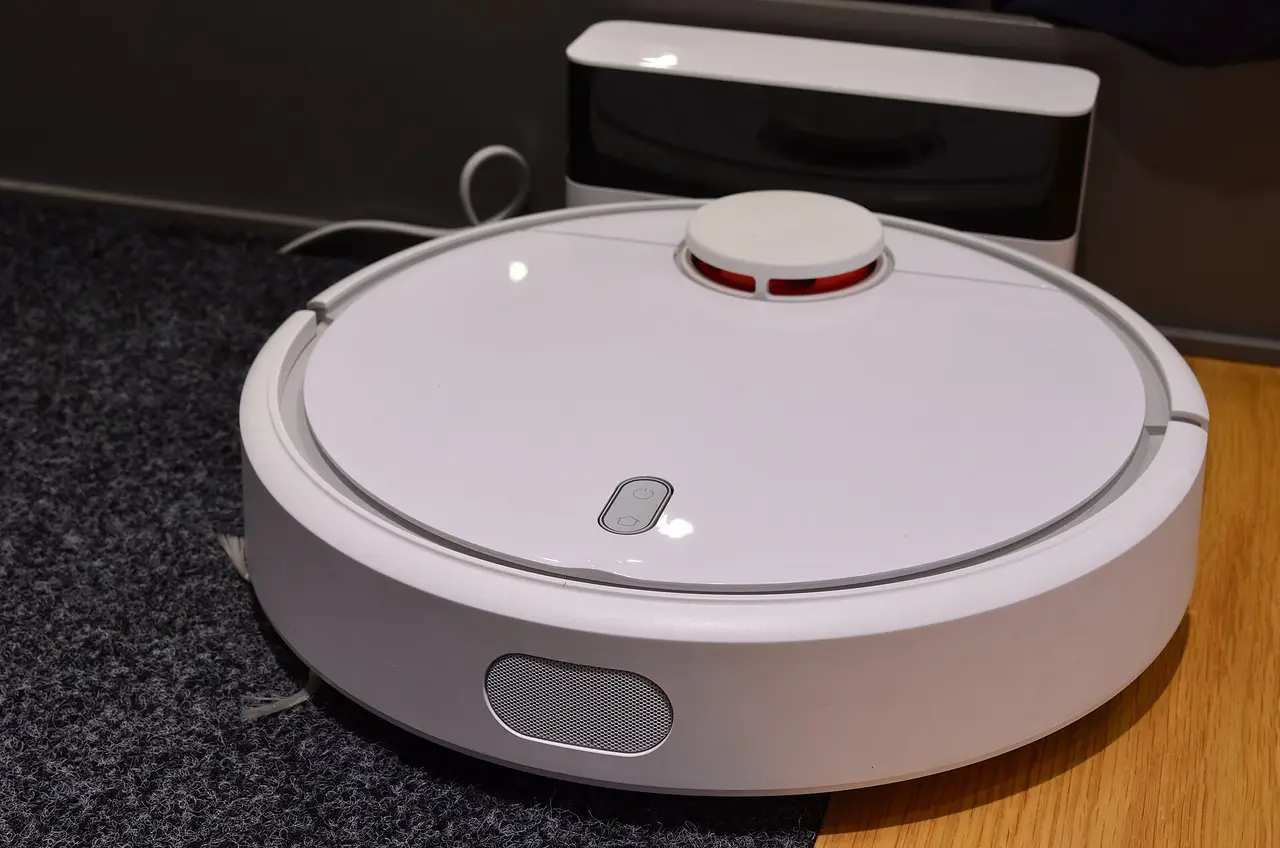 A white round robot vacuum cleaner on a carpet next to its charging dock