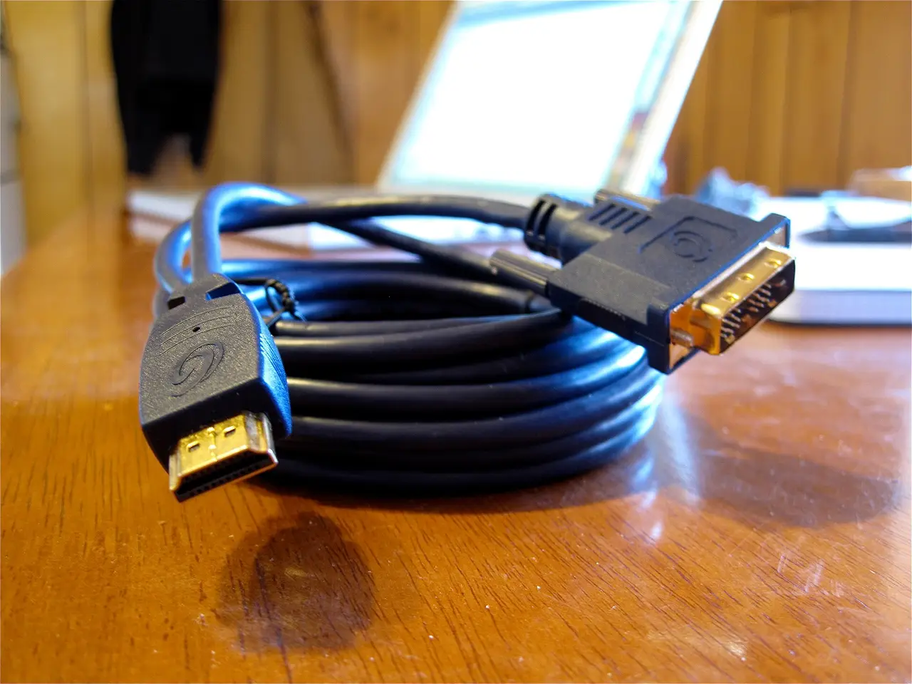 A coiled black video cable with HDMI and DVI plugs on a wooden desk