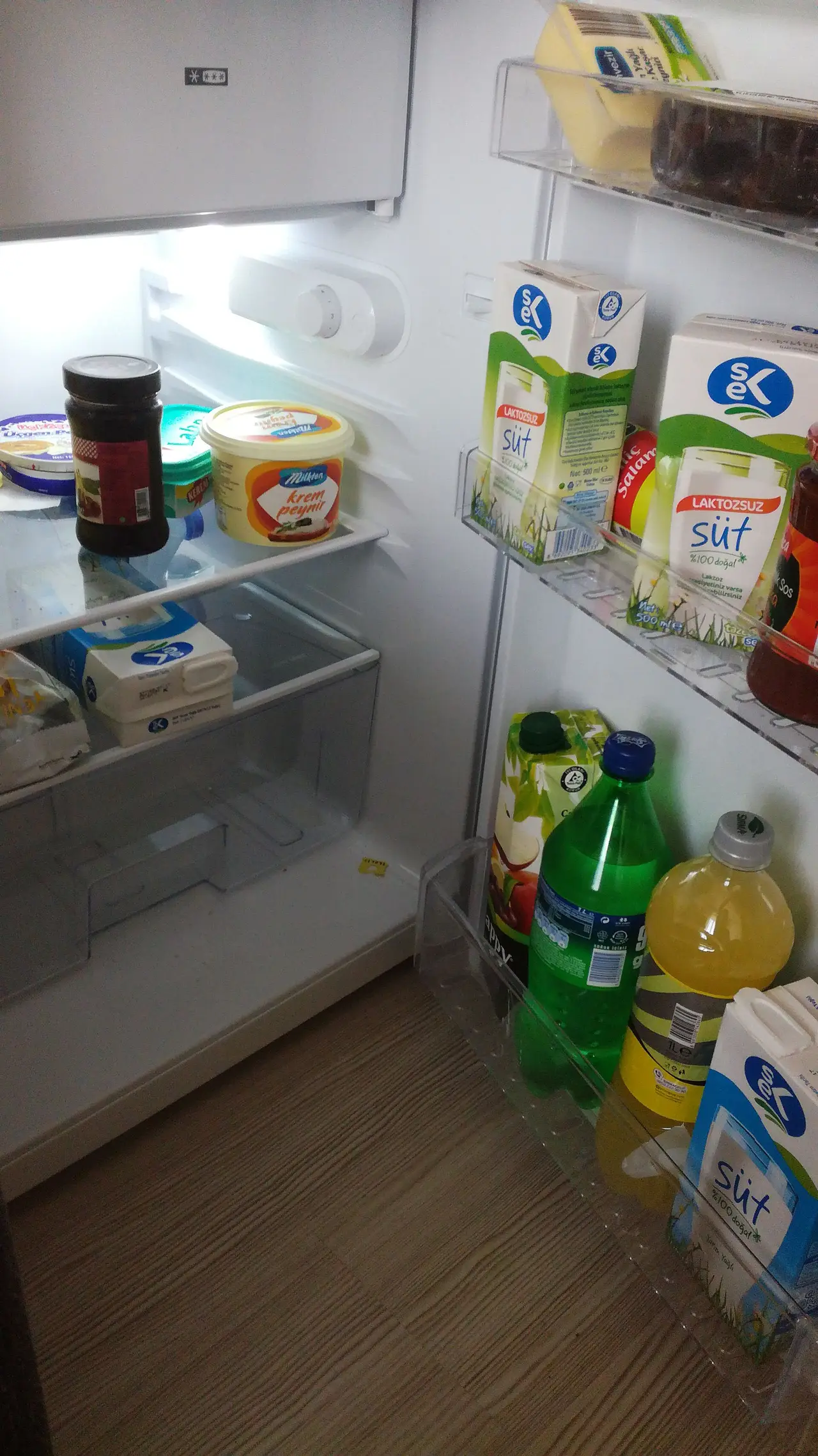 An open mini refrigerator with milk cartons, bottles and jars on its shelves