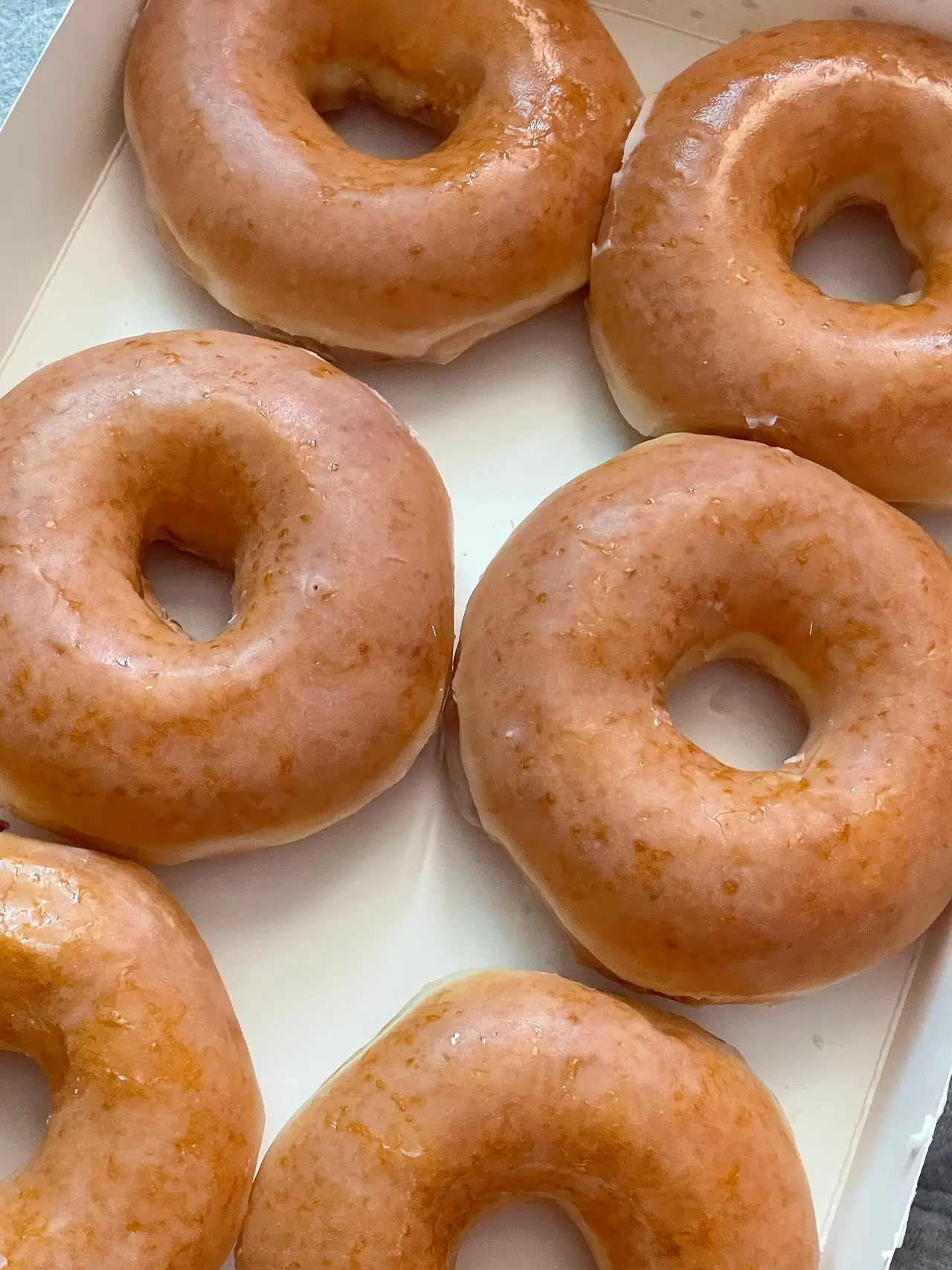 Six glazed ring doughnuts in a white box seen from above