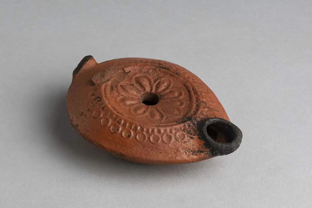 A reddish clay oil lamp with a flower pattern on a grey background