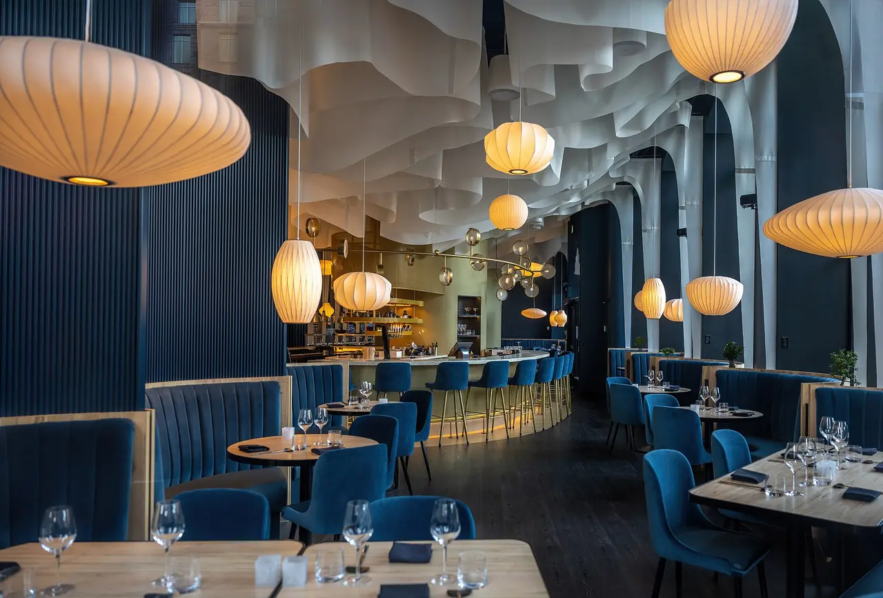 A restaurant interior with blue seating, set tables and hanging paper lamps