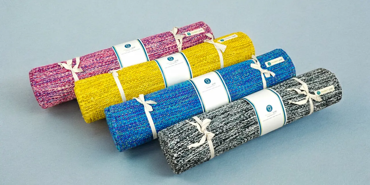 Four rolled yoga mats in pink, yellow, blue and grey tied with white string