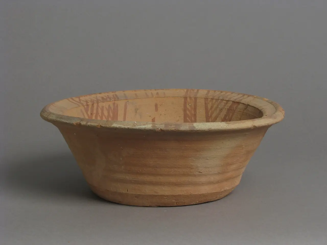 A round clay bowl with a wide rim on a grey background