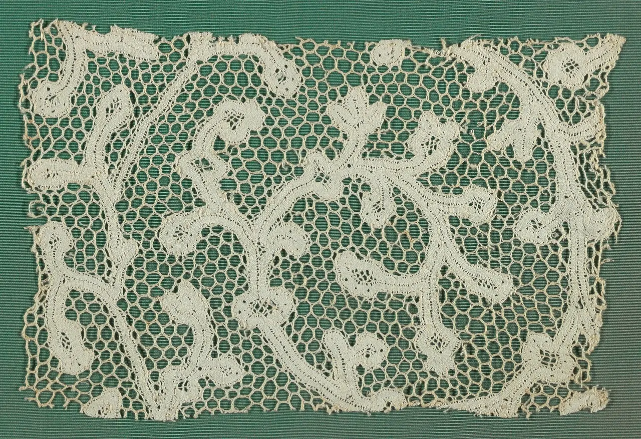 A white bobbin lace fragment with a scrolling vine pattern