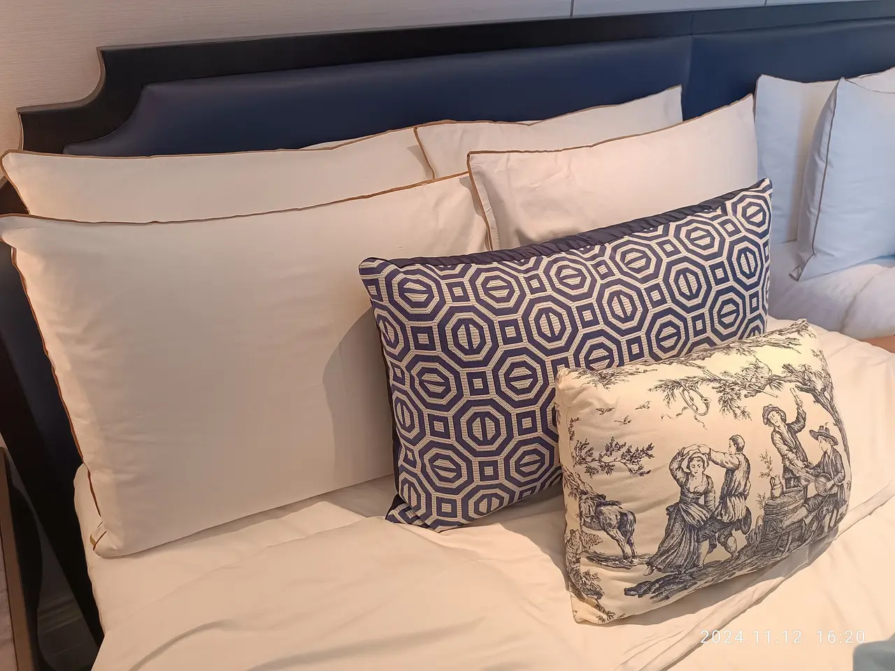 A made bed with several white pillows and two patterned cushions