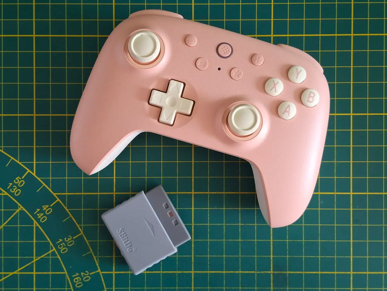 A pink game controller on a green mat with a grey receiver