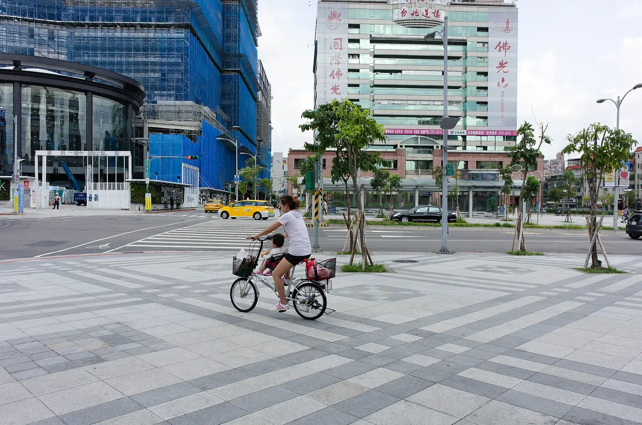 A woman and child on one bicycle crossing a wide paved square