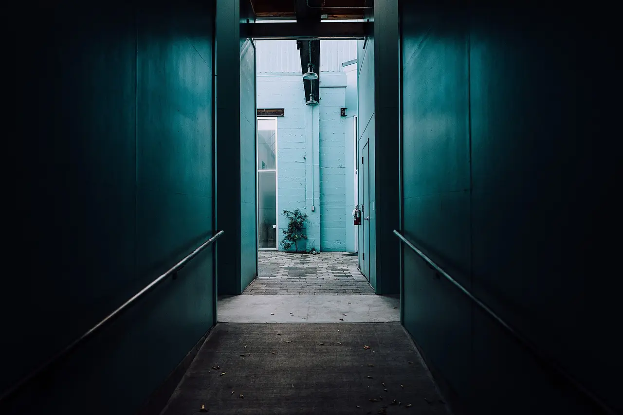 A dark corridor with handrails leading to a bright opening