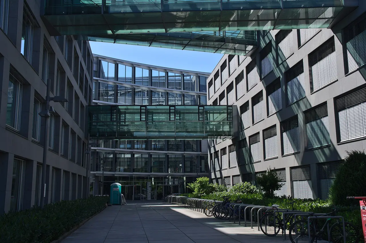 Glass-fronted office wings and a glazed bridge around a paved courtyard