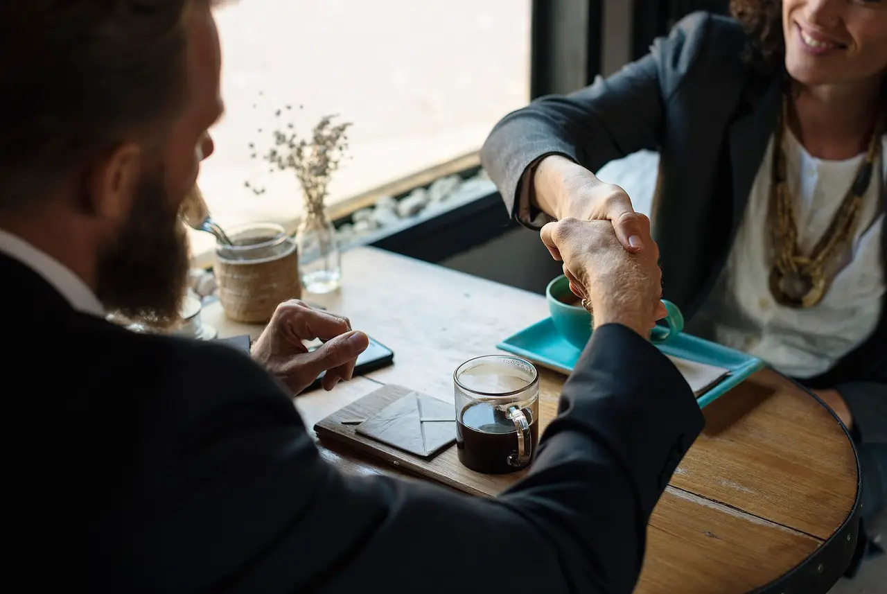 Two people shaking hands over a cafe table with cups and a phone on it