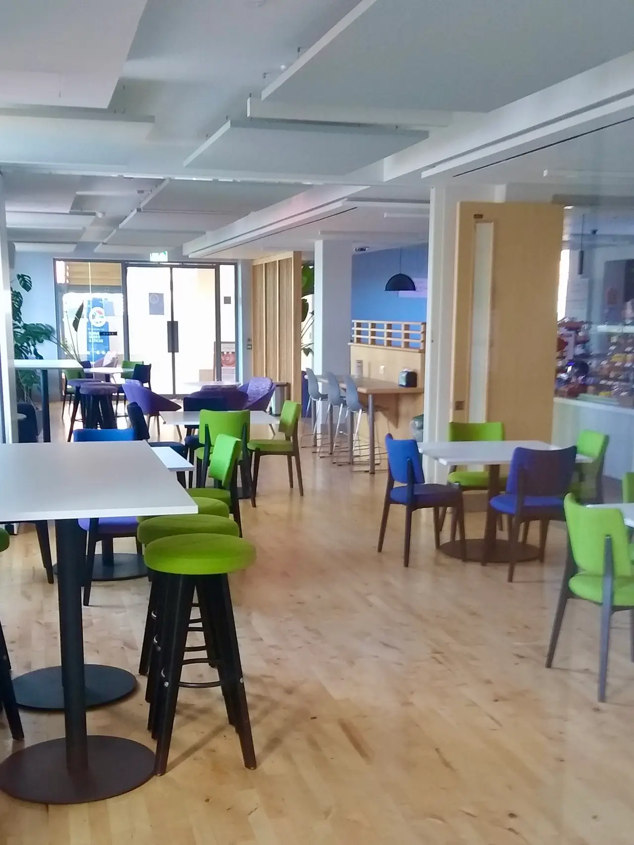 Tables, blue chairs and green bar stools in a bright coffee shop room