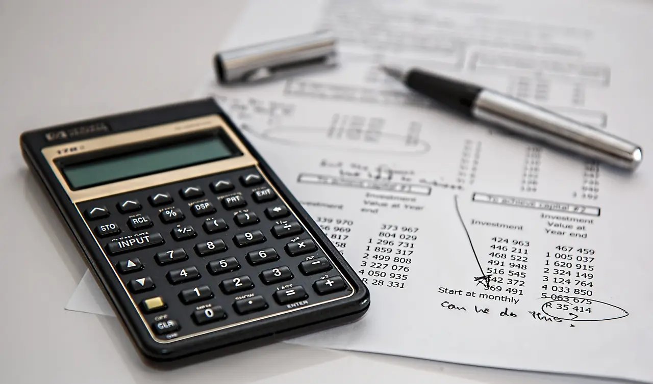 A black calculator on sheets of numbers with a pen lying across them