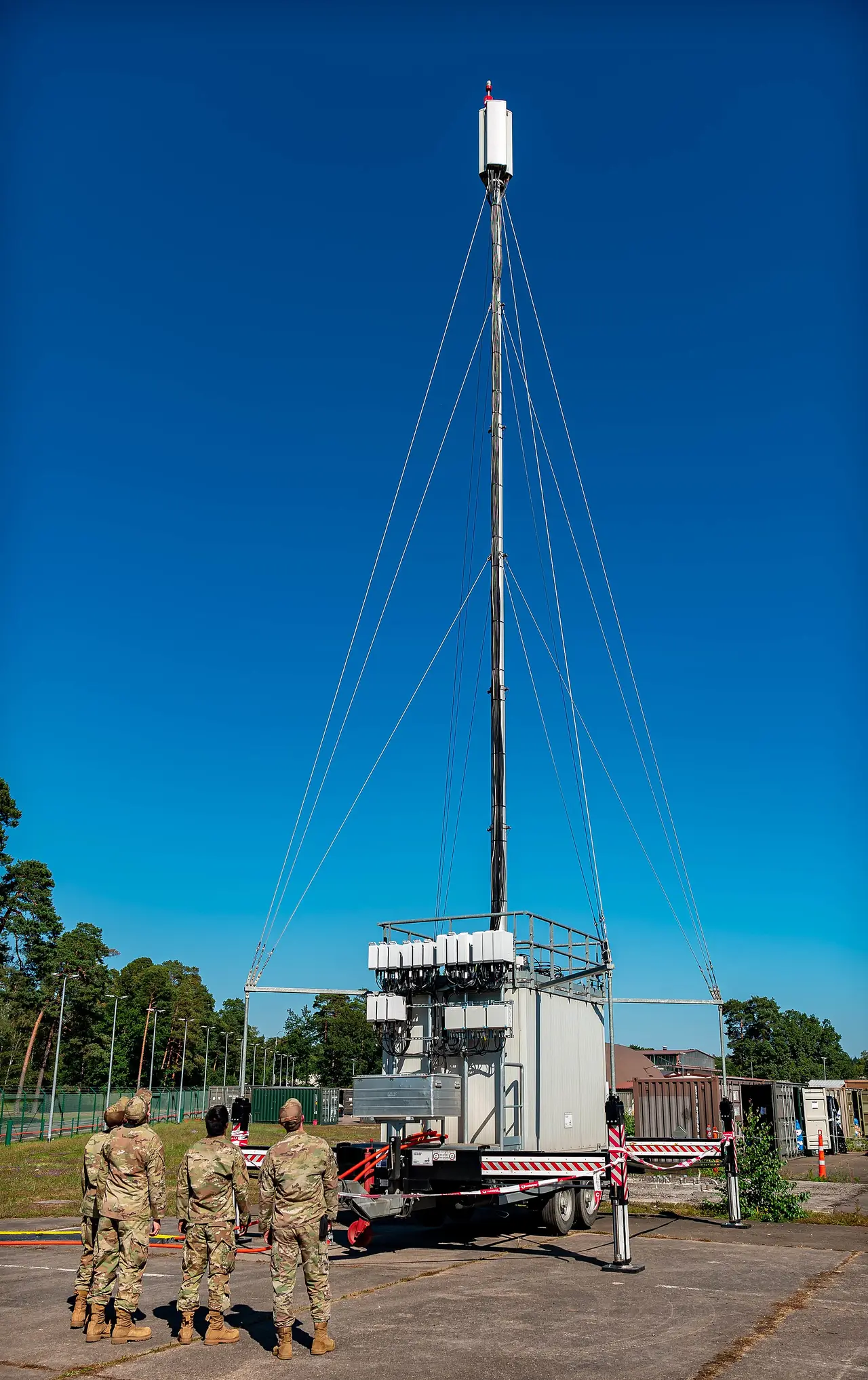 A tall guyed mast on a trailer with soldiers standing beside it