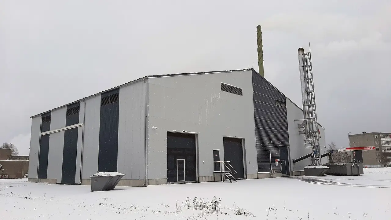 A grey industrial building with a chimney beside snow-covered ground