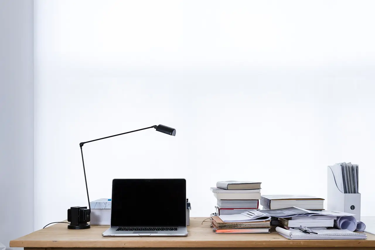 A laptop, books and a desk lamp on a wooden desk