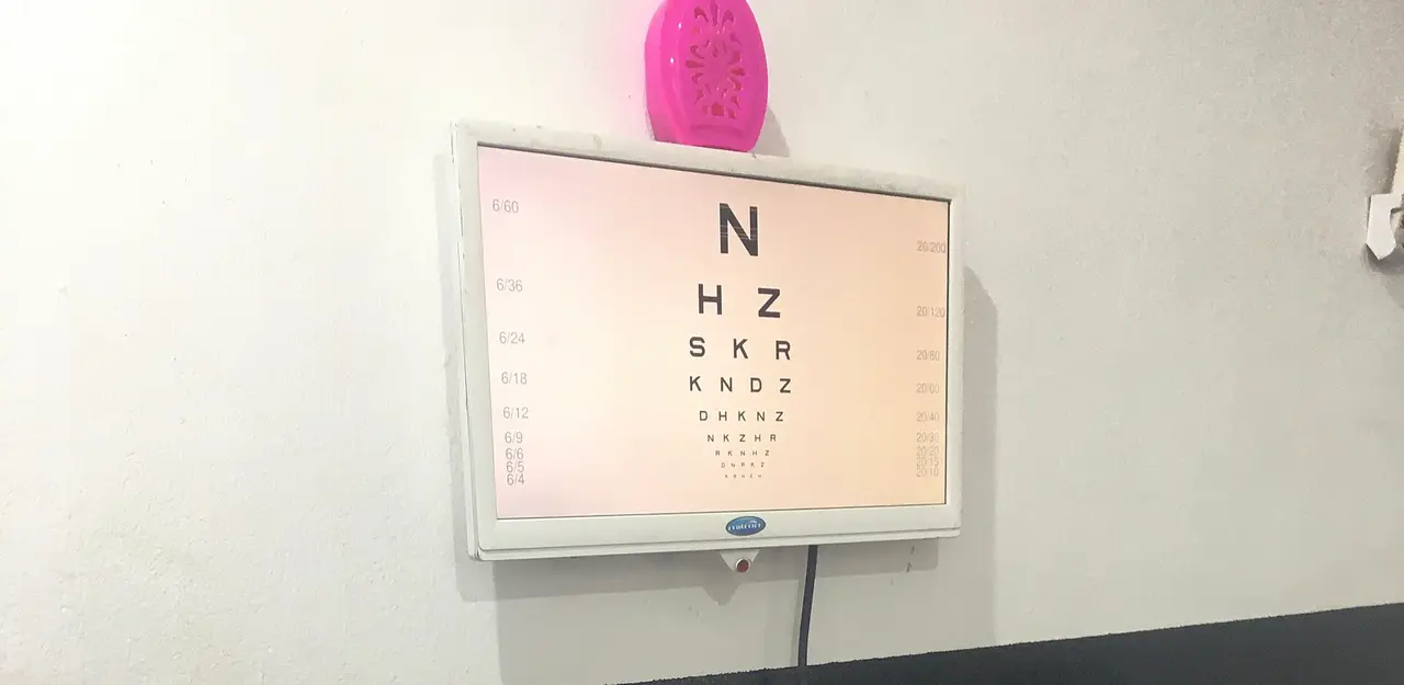 A lit eye test chart with rows of shrinking letters on a white wall