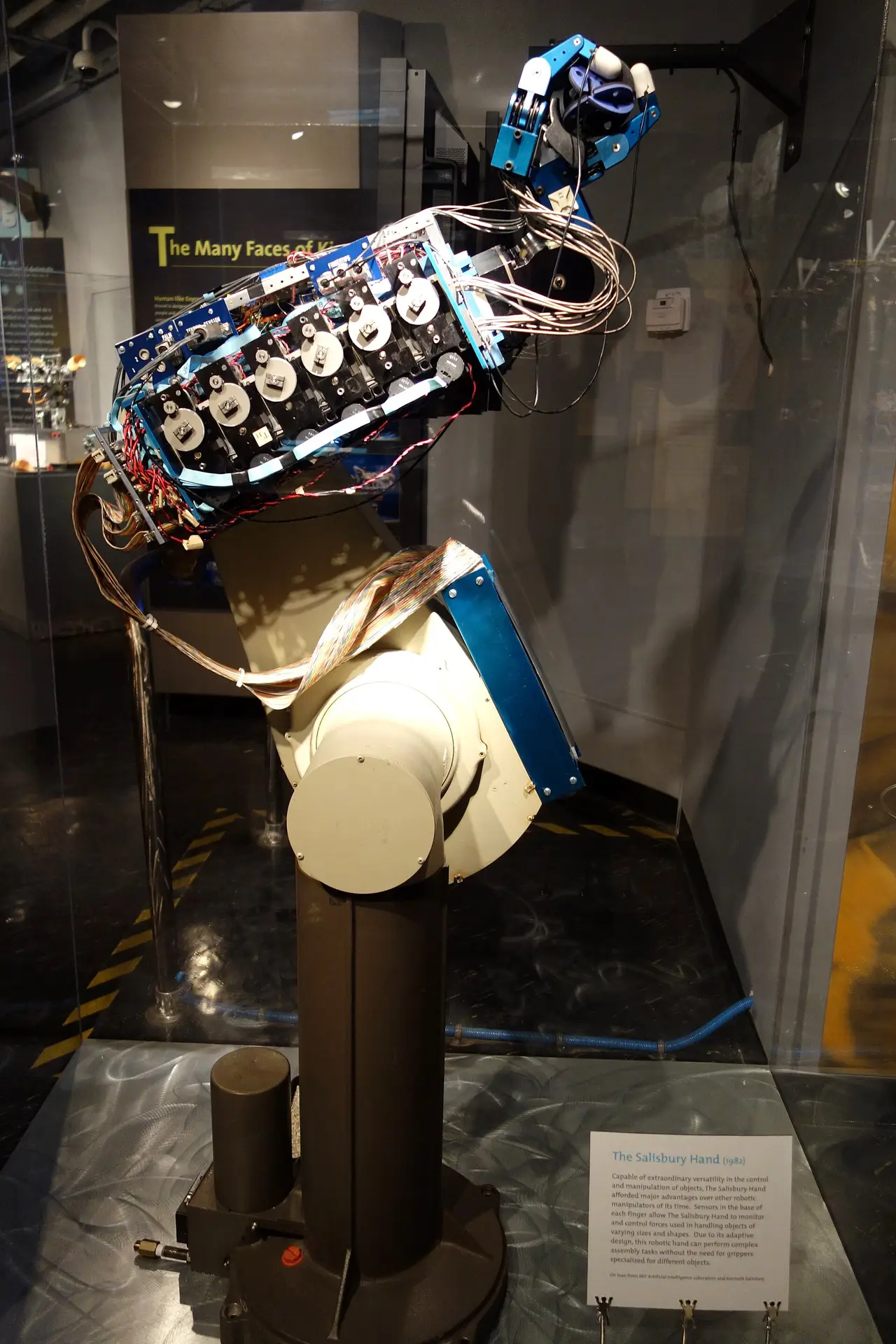 A robotic hand with blue motors and wiring mounted on a stand in a glass case