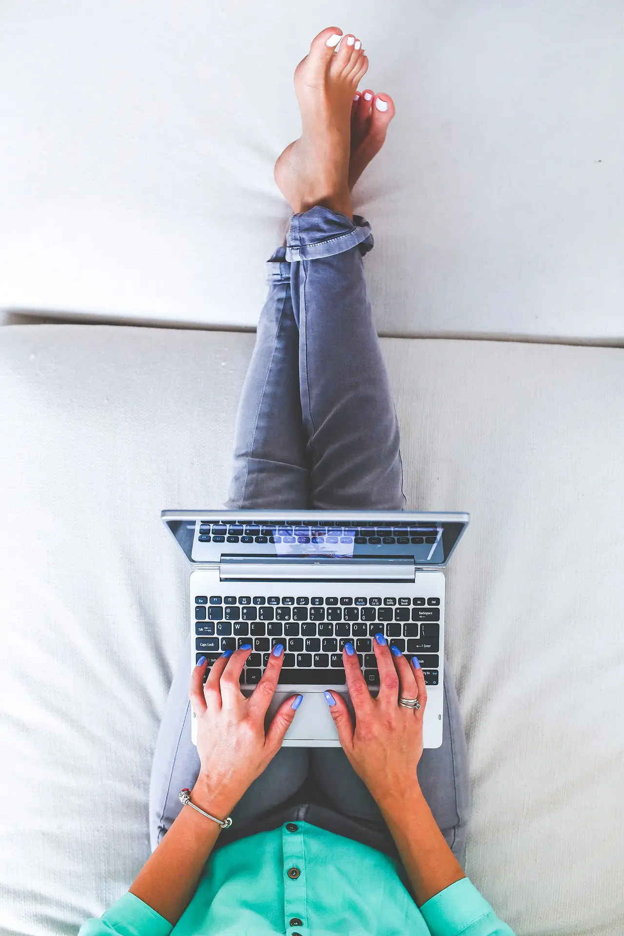 A woman on a white sofa typing on a laptop, seen from above