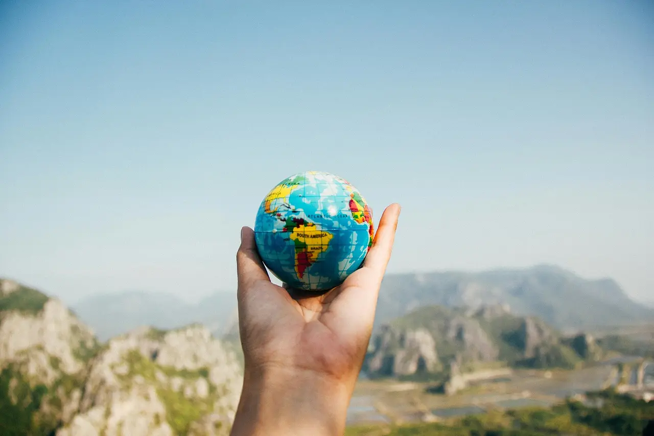 A hand holding a small coloured globe in front of distant mountains