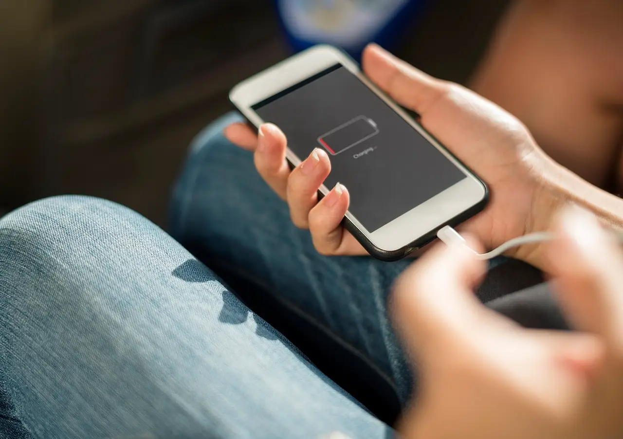 Hands holding a phone showing a flat battery with a cable attached