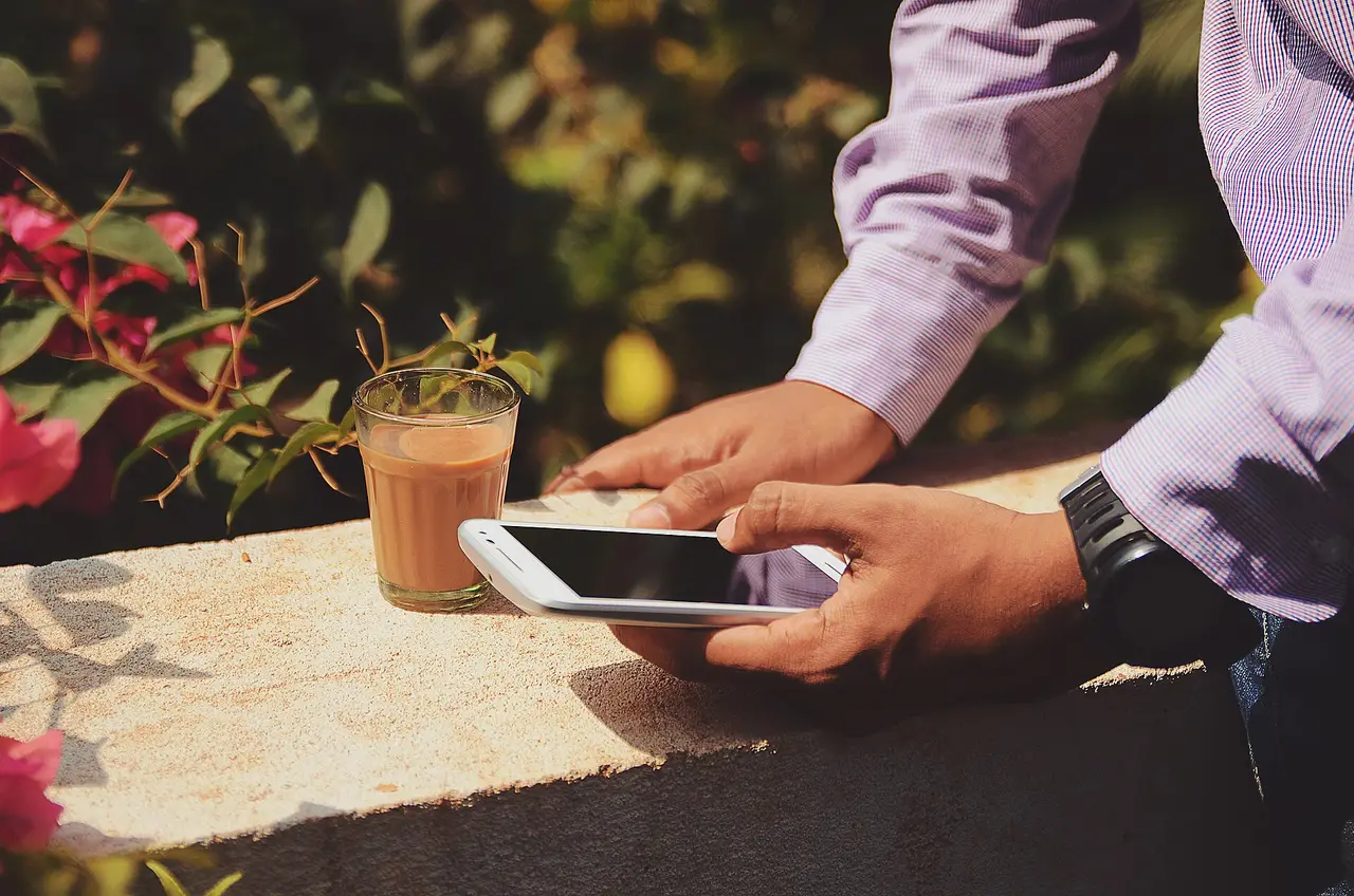 Hands holding a smartphone next to a glass of iced coffee