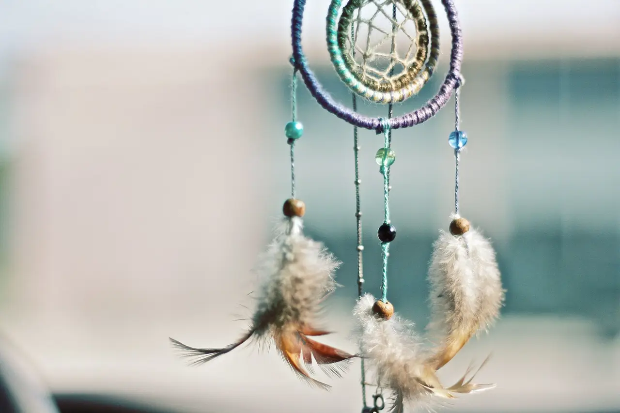 A hanging dreamcatcher with beads and grey and brown feathers against a soft background