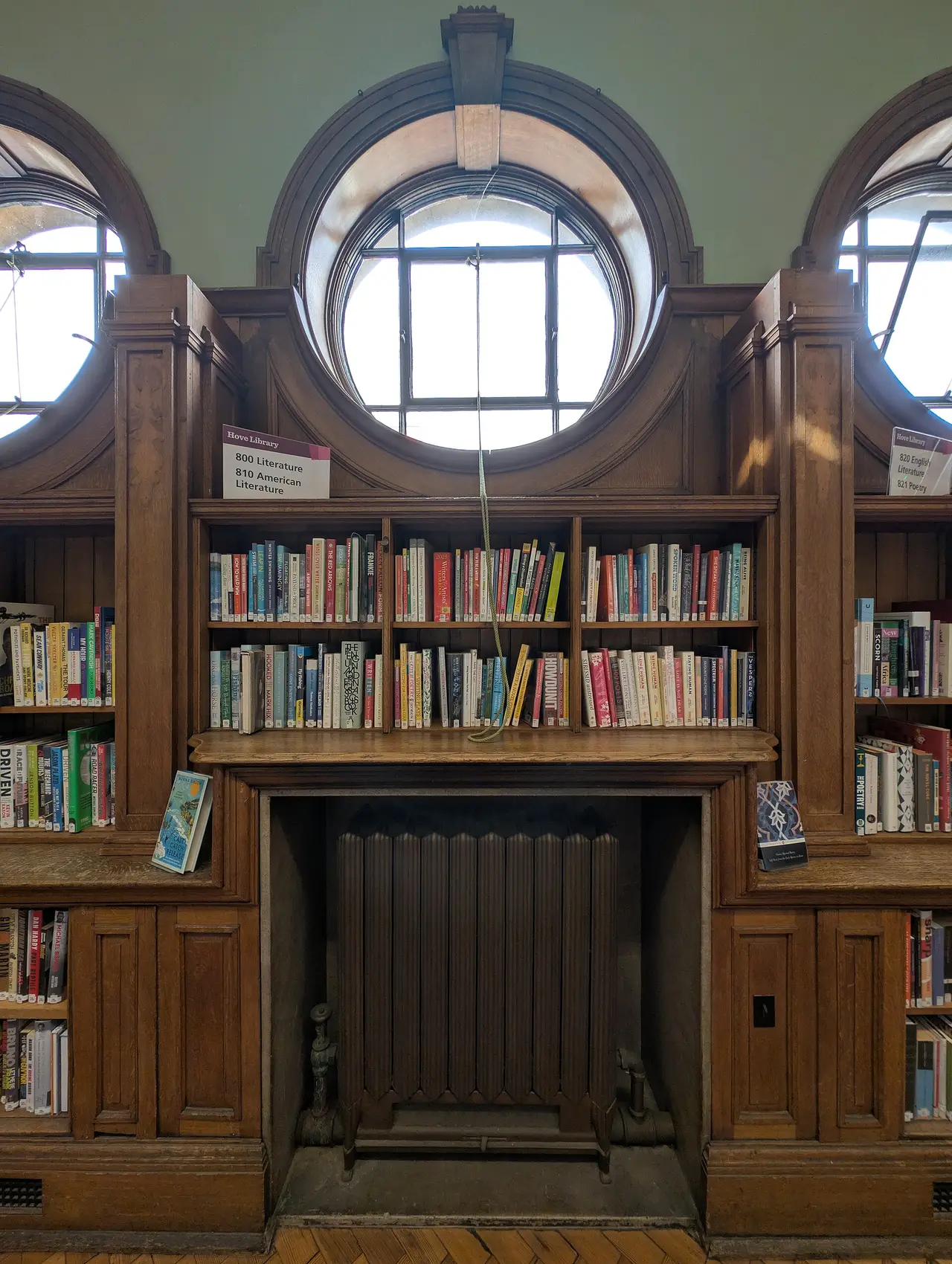 Wooden library shelves of books around a fireplace and round windows