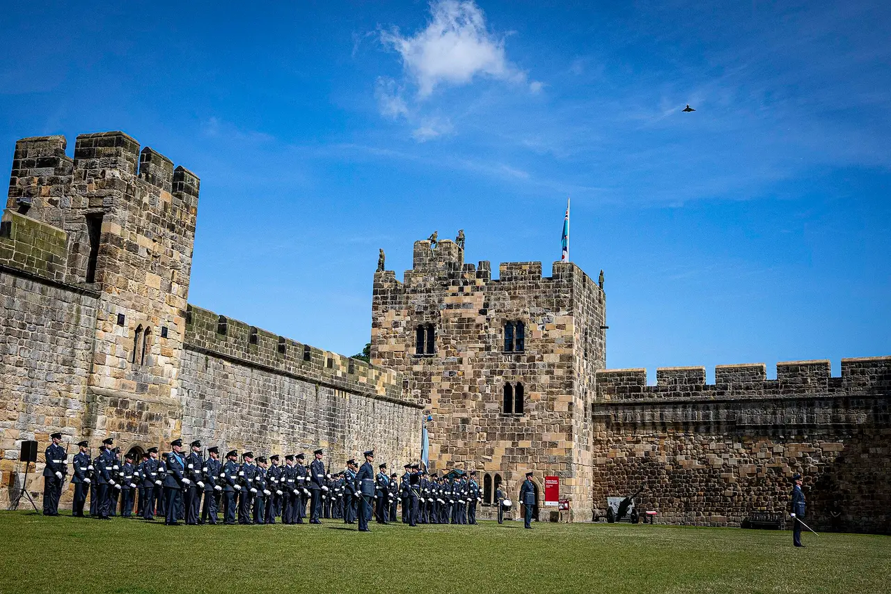 Stone castle tower and walls with uniformed ranks on the grass below