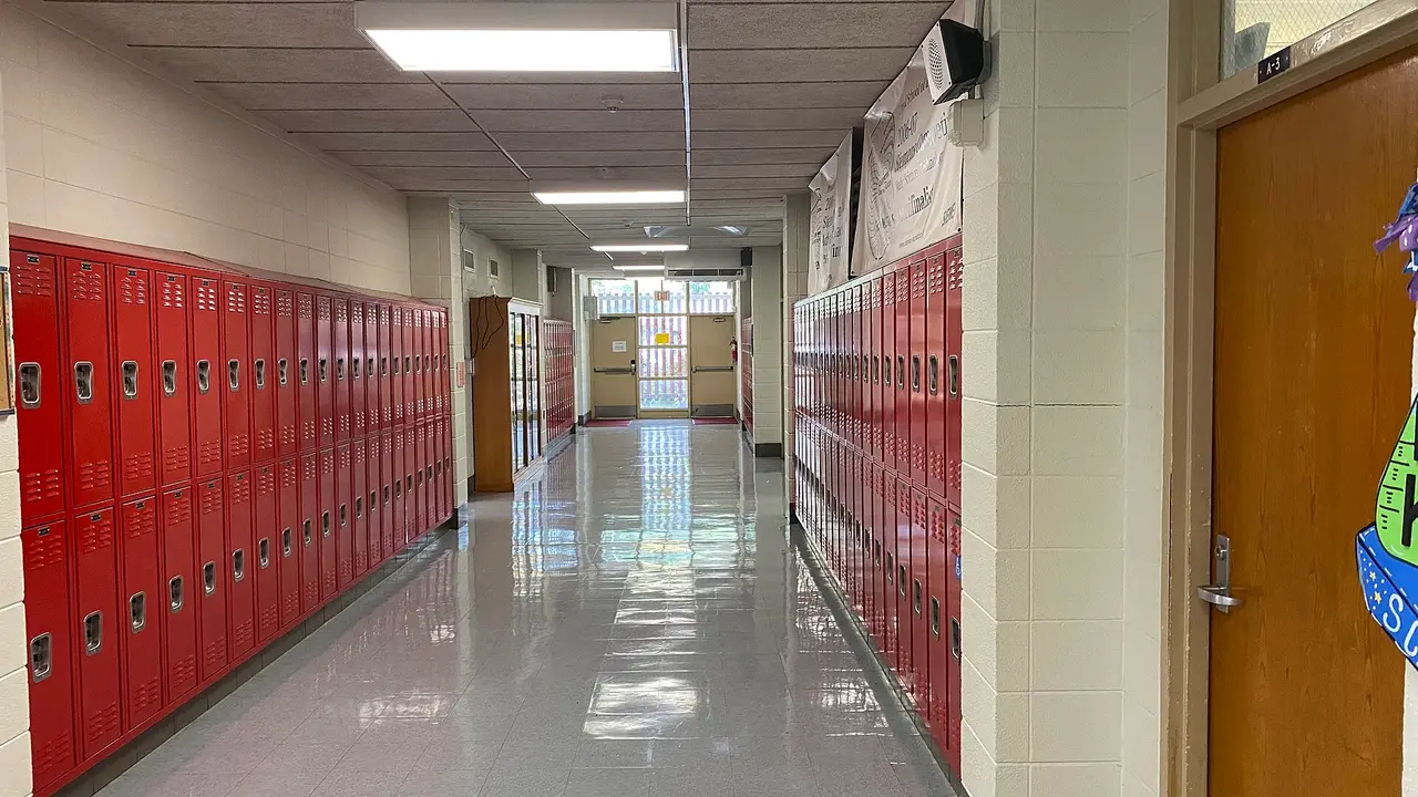 Rows of red metal lockers along a polished school hallway under ceiling lights