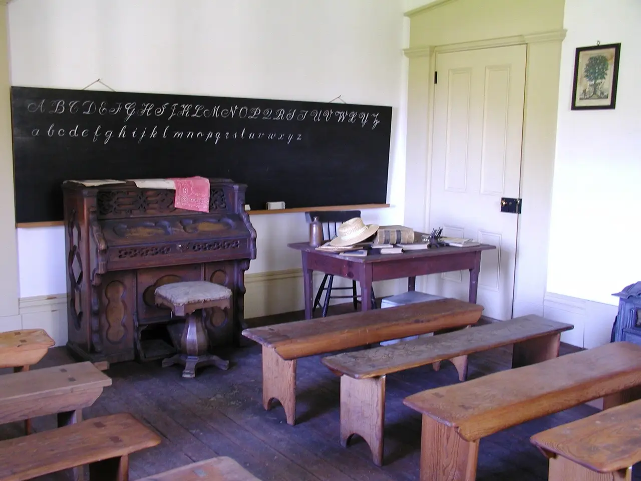 A schoolroom with wooden benches, an organ and a blackboard